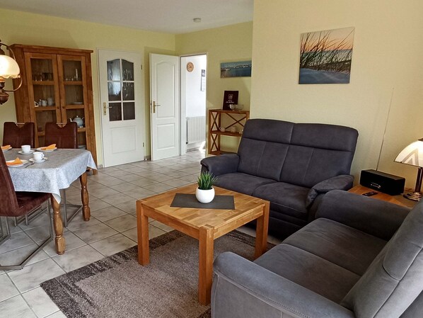 Una sala de estar con un sofá, una mesa de comedor con sillas, una mesa de centro de madera y un mueble aparador con puertas de cristal.