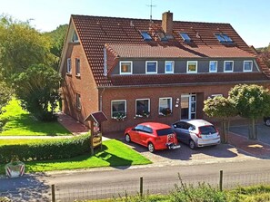 A two-story house with a red car parked in the driveway and a white car parked in the garage.