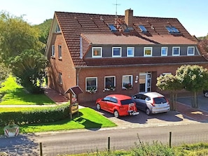 Una casa de dos pisos con un coche rojo estacionado en la entrada y un coche blanco en el garaje.