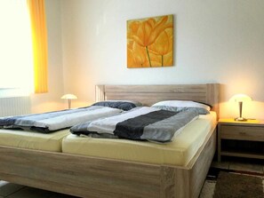 Una cama doble con cabecera de madera, dos lámparas de noche y un cuadro de flores en la pared.