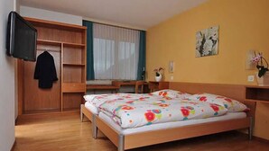 Een slaapkamer met een houten bed, een aan de muur bevestigde televisie, een bureau en een raam met gordijnen.