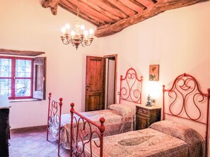 Une chambre avec deux lits, un lustre, un plafond en bois et une fenêtre avec des volets rouges.