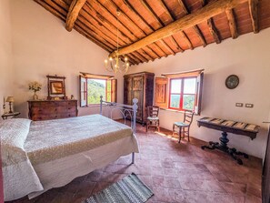 A bedroom with a bed, dresser, two chairs, a table, and a window with a view.