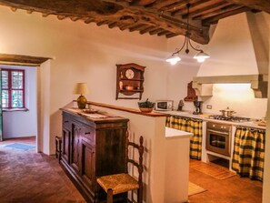 A kitchen with a wooden island, a clock, a microwave, a stove, and a window.