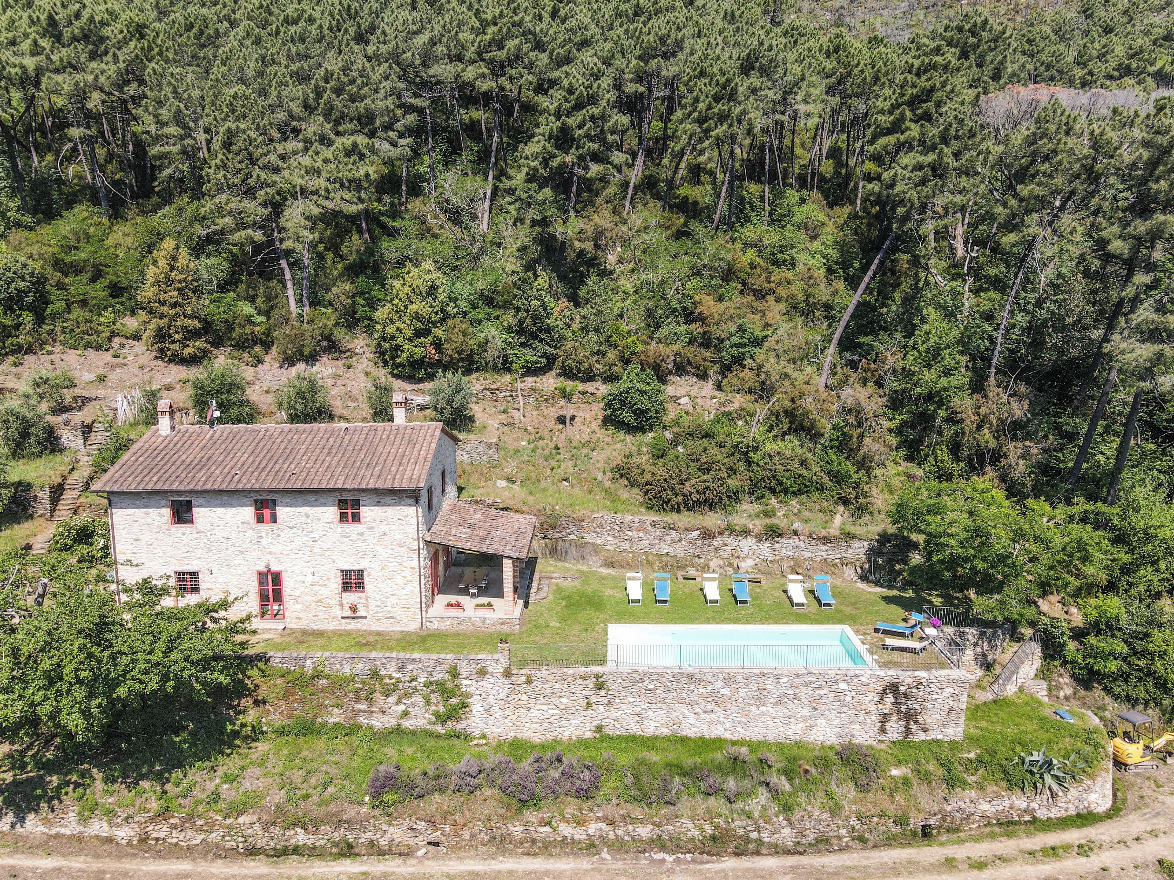 A stone building with a tiled roof, a swimming pool, and a few lounge chairs.