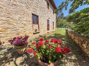 A stone building with a swimming pool and potted flowers in the foreground.