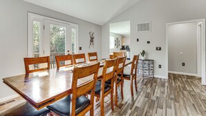 A dining area with a wooden table and chairs, a kitchen in the background, and a view of trees through the windows. - Home < 2 Mi to Mtn Greens Golf, Massanutten Ski! (Mcgaheysville)