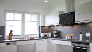 Een moderne keuken met witte kasten, een vaatwasser, een fornuis en een raam dat natuurlijk licht binnenlaat.