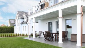 Een ruim terras met een eettafel en stoelen, een overdekt gedeelte met een tafel en stoelen, en uitzicht op omliggende huizen.