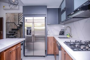 Une cuisine moderne équipée d’un réfrigérateur en acier inoxydable, d’une cuisinière à gaz et de meubles de rangement en bois.