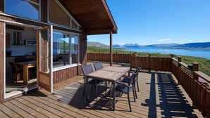 A wooden deck with a table and chairs, overlooking a scenic view of a lake and mountains. - Brekka - Stunning Country & Ocean View Location, Yet Close To Reykjavik (Akranes)