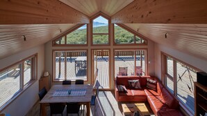 A cozy interior with a wooden ceiling, large windows, a dining area, and a red sofa. - Brekka - Stunning Country & Ocean View Location, Yet Close To Reykjavik (Akranes)