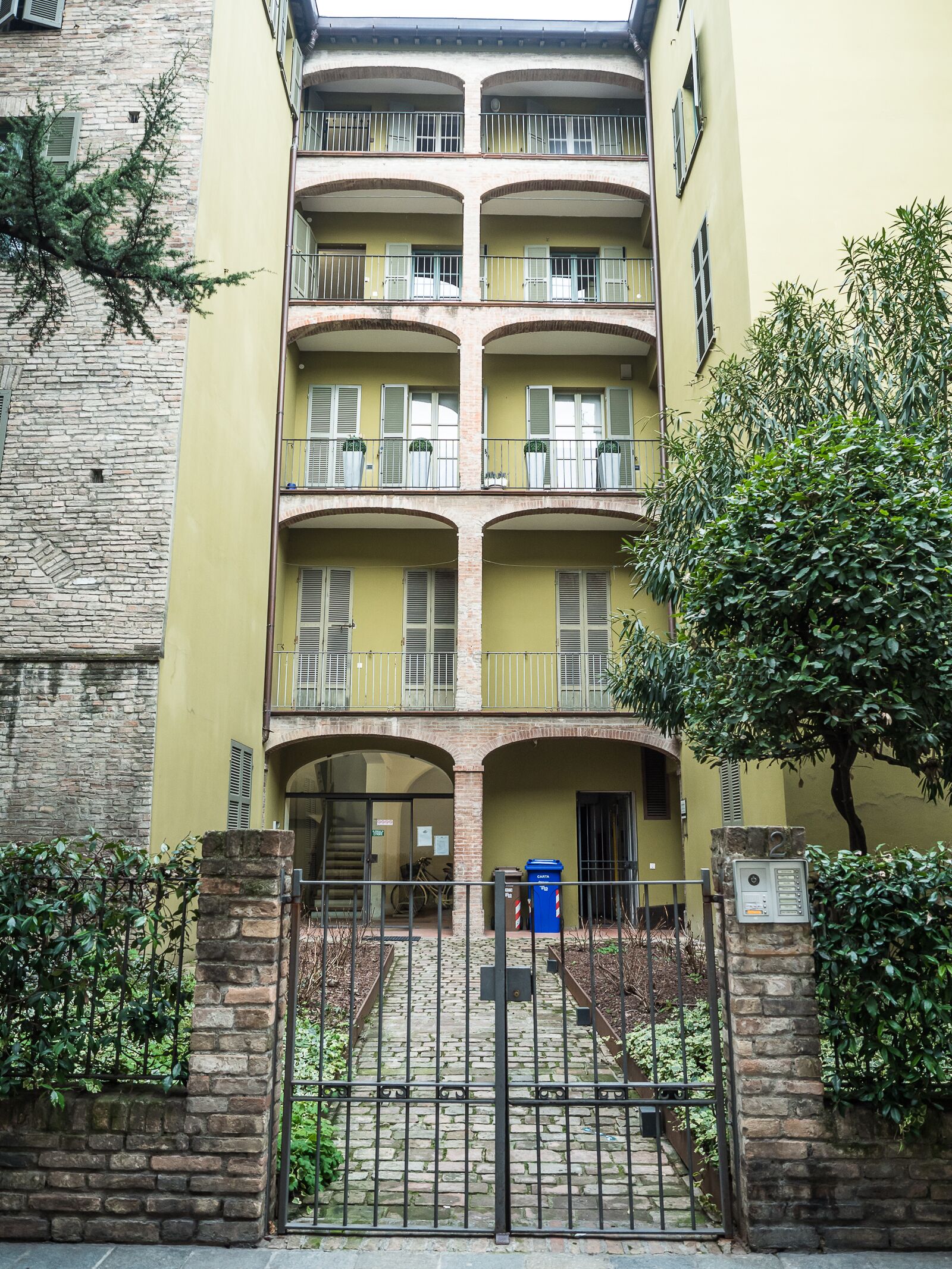 A multi-story building with balconies, a stone facade, and a gated entrance.