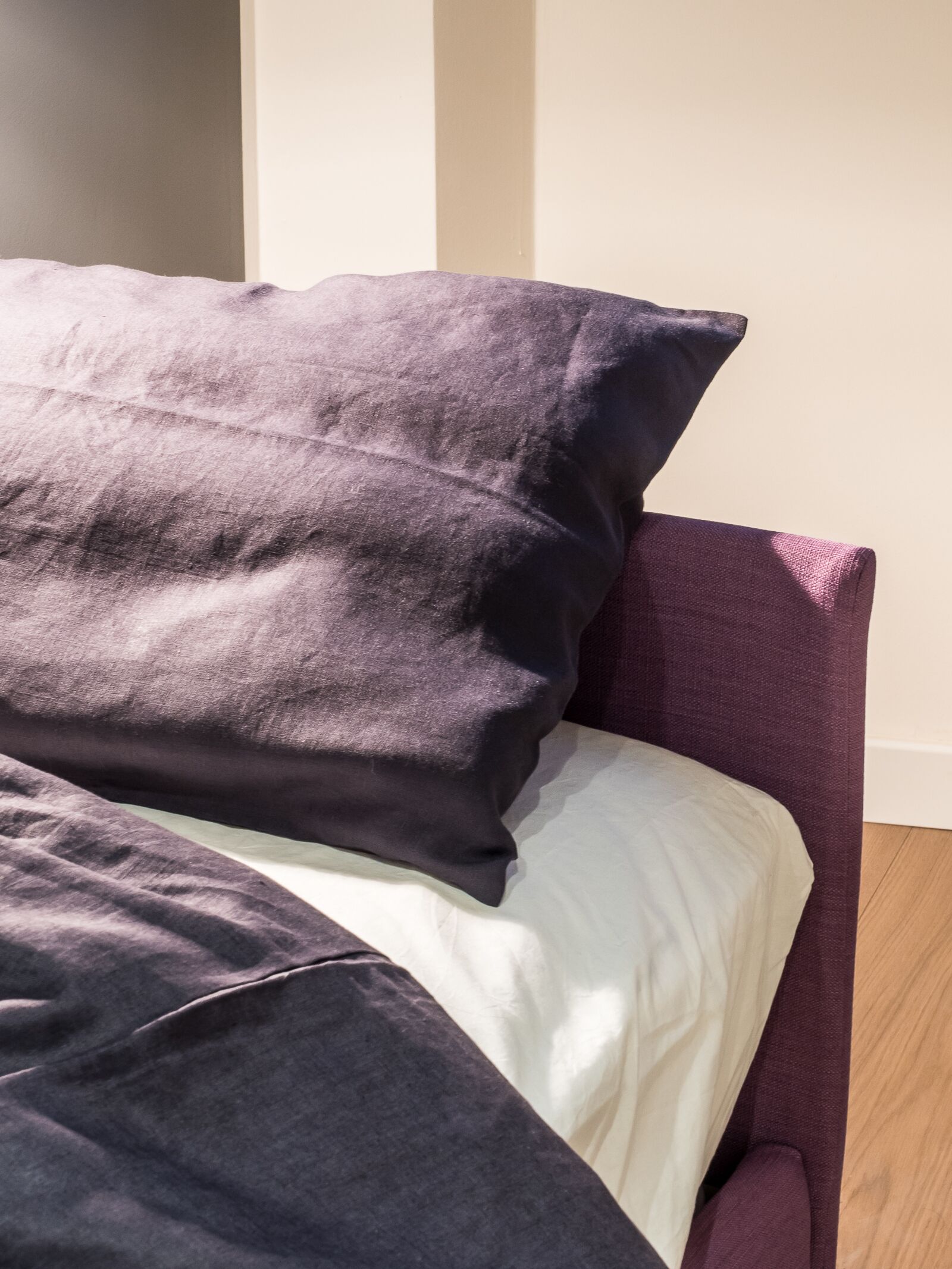 Uma cama com colchão branco e duas almofadas escuras.