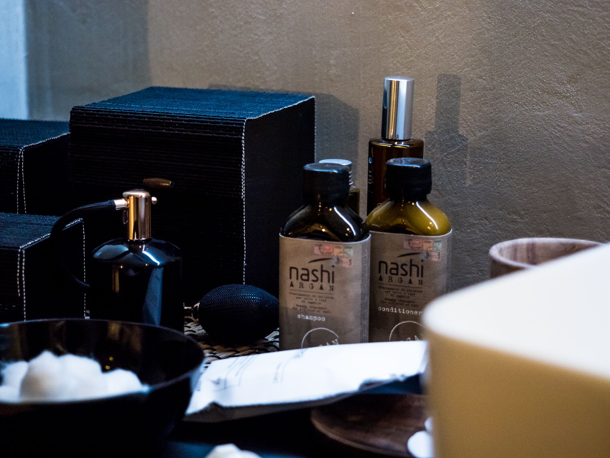 Une salle de bain avec un lavabo noir, deux bouteilles de shampoing Nashi Argan, un distributeur de savon noir et un bol blanc.
