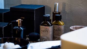 Une salle de bain avec un lavabo noir, deux bouteilles de shampoing Nashi Argan, un distributeur de savon noir et un bol blanc.