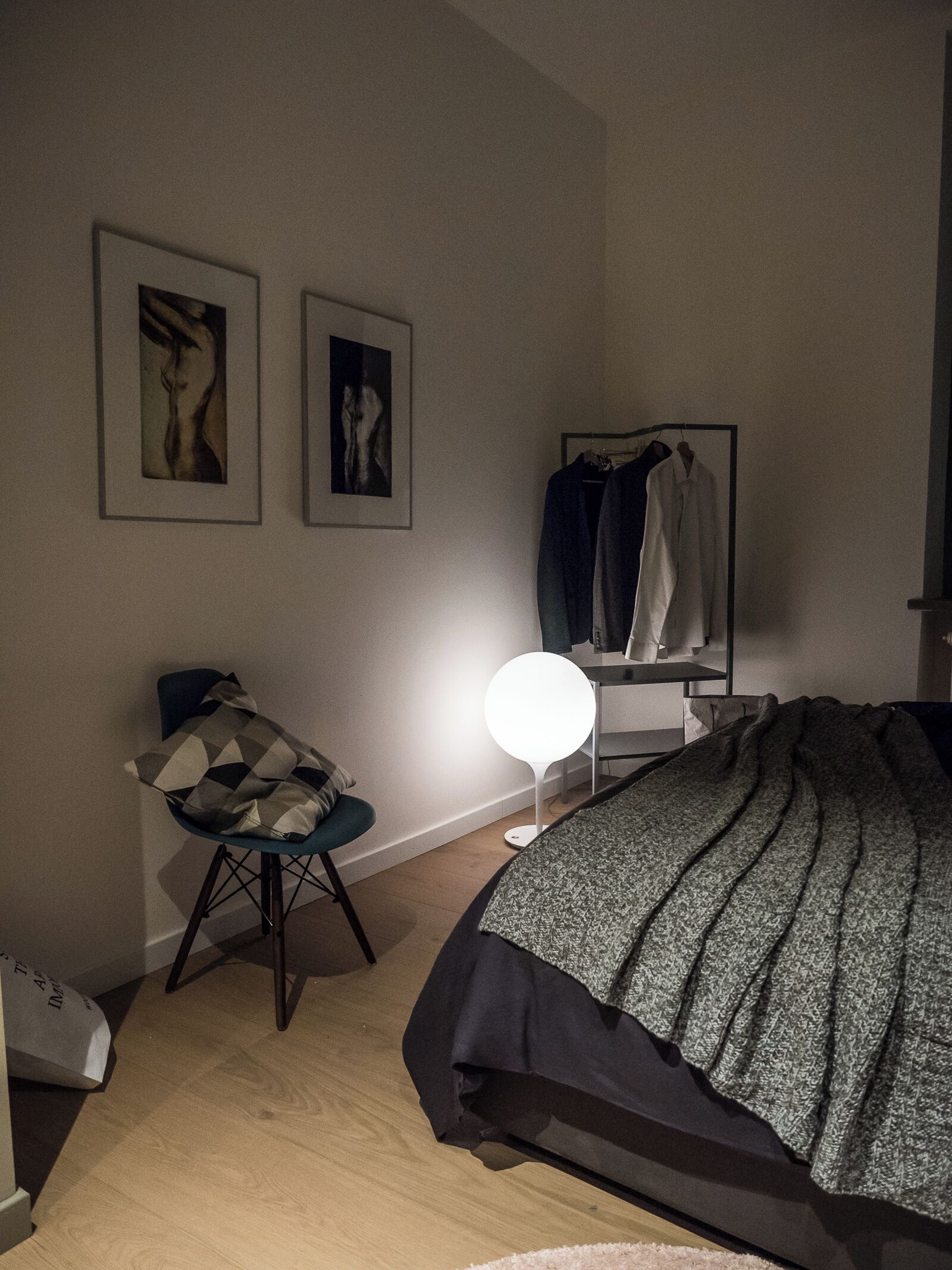 Une chambre à coucher avec un lit, une chaise, un bureau et une armoire. Deux tableaux encadrés sont accrochés au mur.
