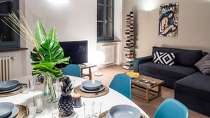 A modern living room with a dining area, a tall bookcase, and a large abstract painting on the wall. - Le Logge 2 apartment (Parma)