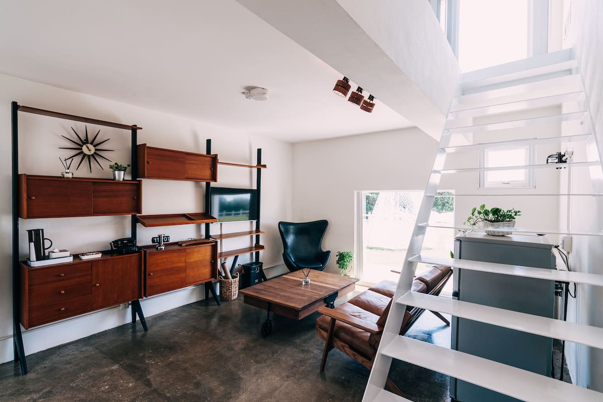 A modern living room with a wooden cabinet, a black leather chair, a wooden coffee table, and a television.