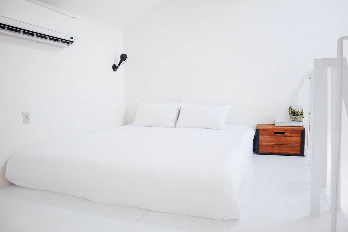 A minimalist bedroom with a large bed, a bedside table with a plant, and a wall-mounted air conditioner.