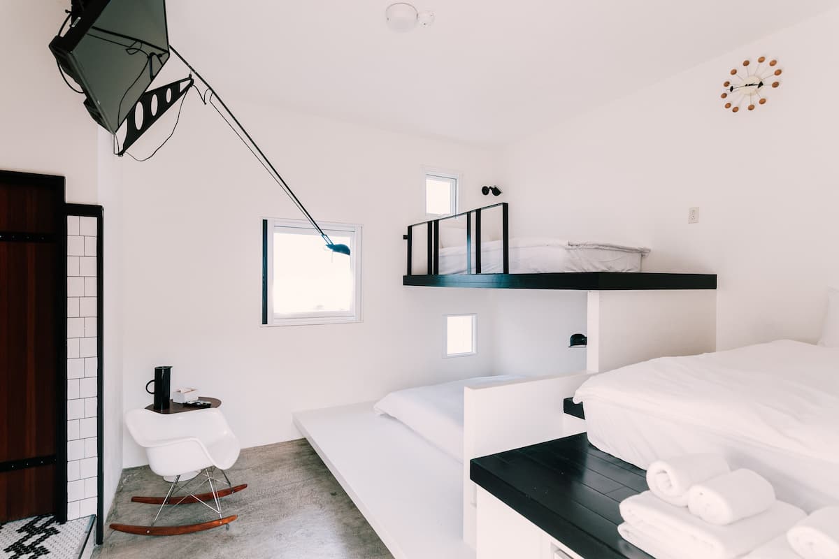 A modern, compact room with a bunk bed, a small desk with a chair, a window, and a clock on the wall.
