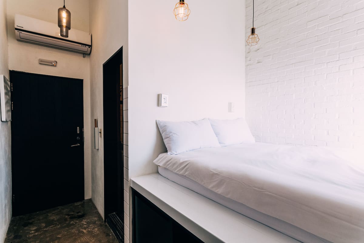 A bedroom with a white bed, a black door, and a white brick wall.