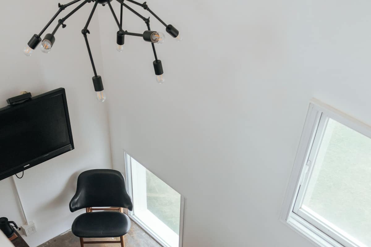 A room with a black chair, a white chair, a TV mounted on the wall, and a staircase.