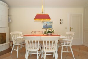 Un coin repas avec une table et quatre chaises, une lampe rouge et dorée, un tableau représentant un voilier et une horloge murale.