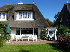 Une maison avec un toit de chaume, des murs extérieurs blancs et un patio couvert avec une table et des chaises.