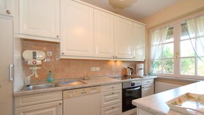 A kitchen with white cabinets, a dishwasher, an oven, and a window with curtains. - House Tondernhüs, Germany (Sylt-Ost)