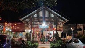 A restaurant with a signboard, outdoor seating, and a car parked in front.