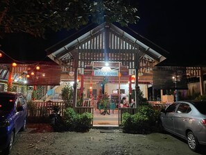 A restaurant with a signboard, outdoor seating, and a car parked in front.