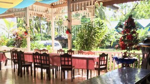 An outdoor patio with wooden tables and chairs, covered by a canopy. - Oasis Resthouse (San Agustin)