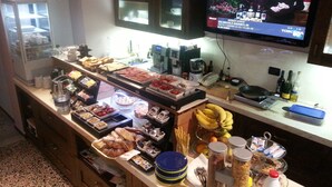A buffet with various food items and a television displaying a news program. - Michele Guest House (Pisa)