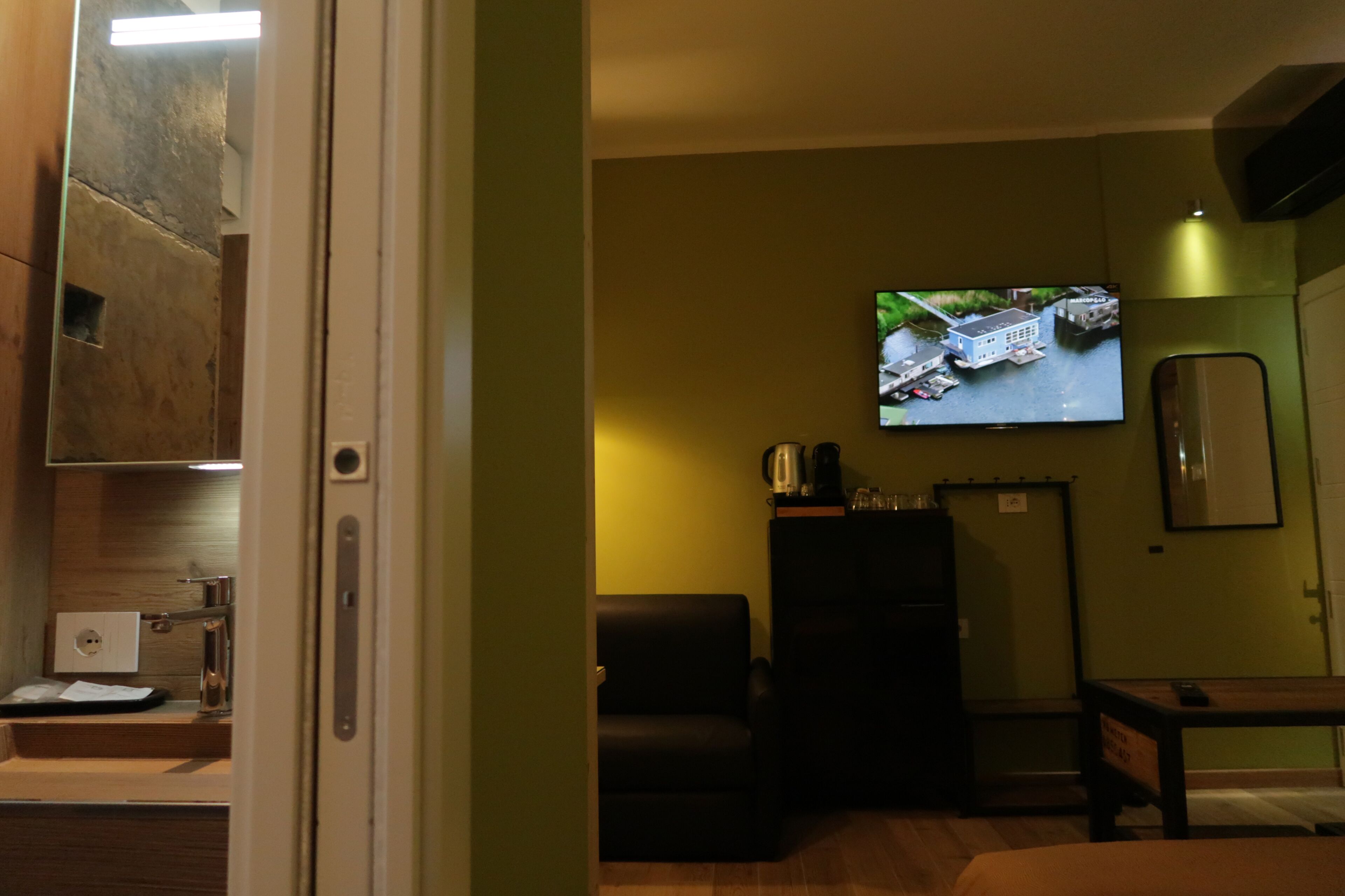 A hotel room with a television mounted on the wall, a sofa, a table, and a cabinet.