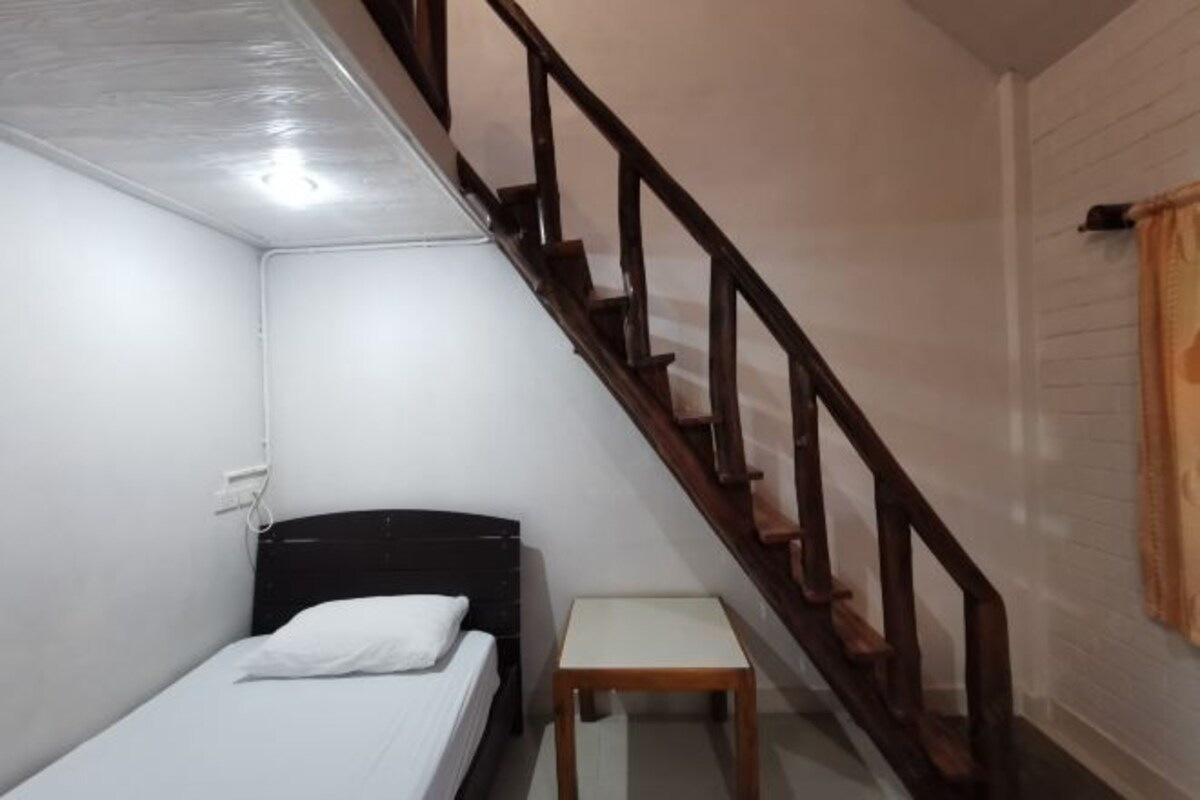 Quarto pequeno com uma cama de solteiro, escada de madeira e uma mesinha.