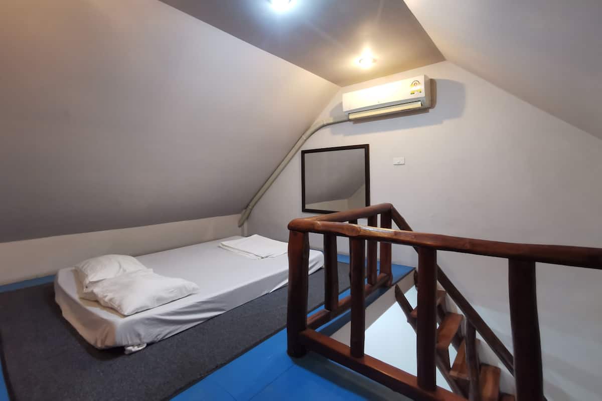 Een kleine eenpersoonskamer met een houten trap, een plafondlamp en een airconditioning.