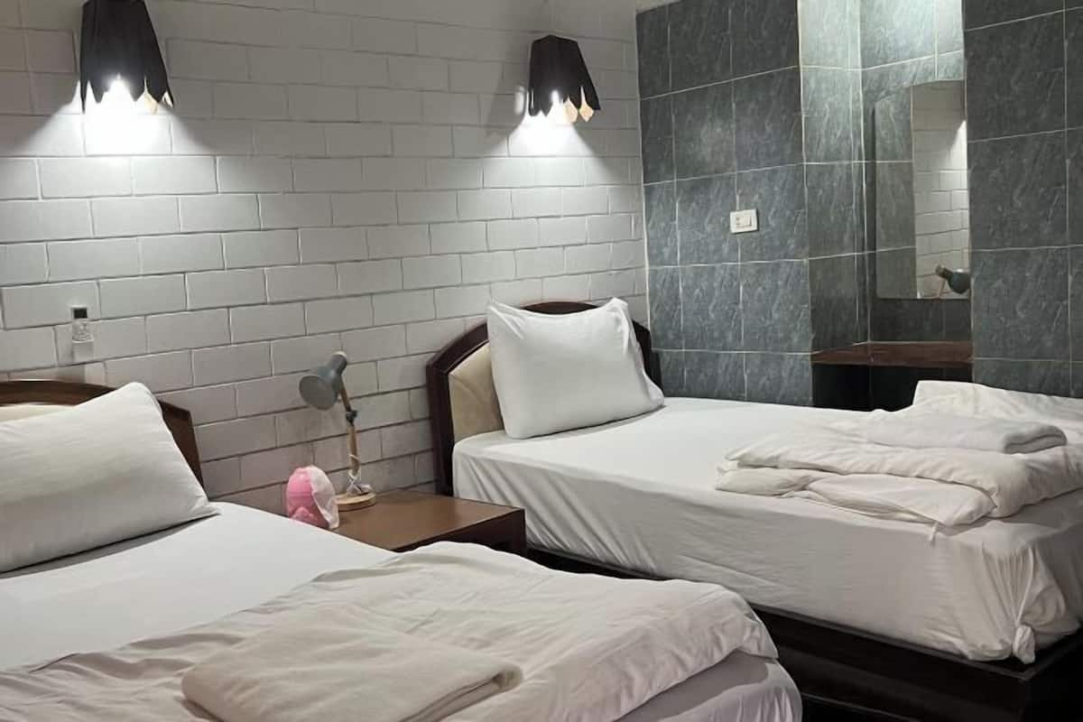 Een hotelkamer met twee bedden, een nachtkastje met een lamp, een spiegel en een muur met een bakstenen patroon.