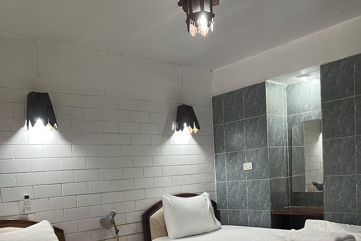 Een hotelkamer met twee bedden, een nachtkastje met lamp, een spiegel en een kroonluchter.