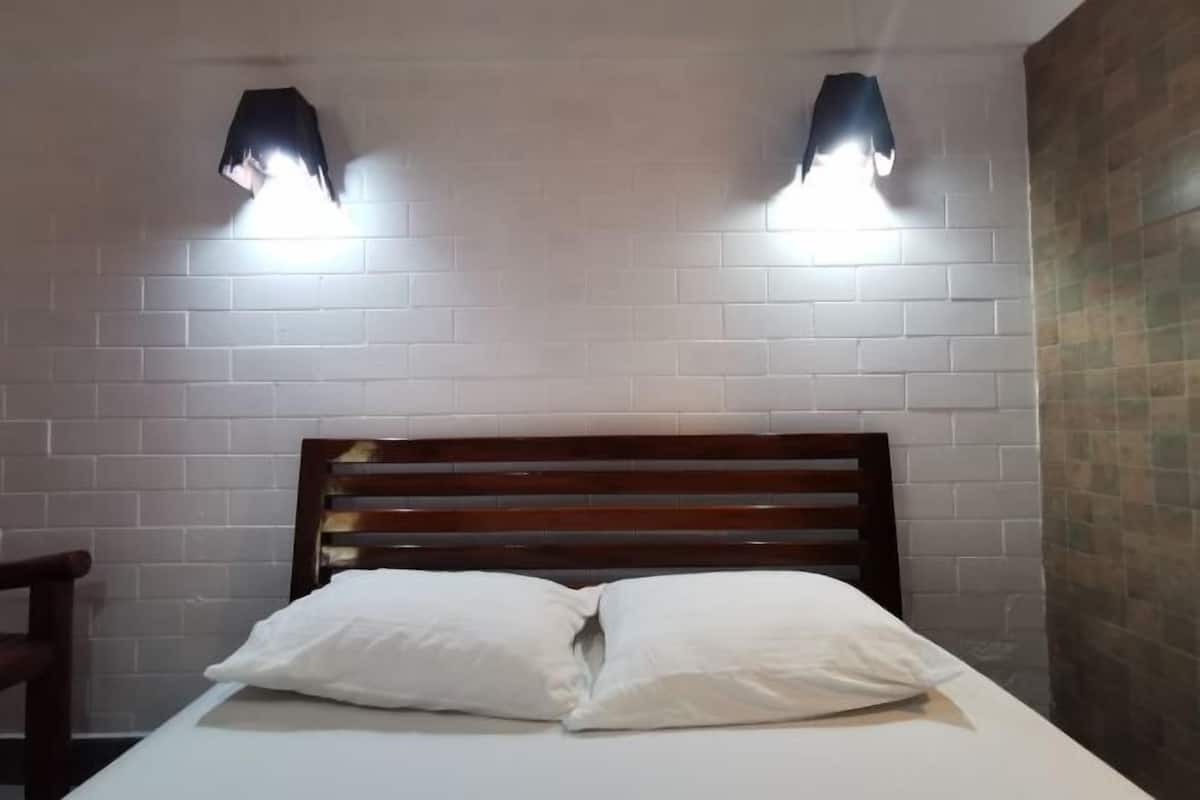 Een kamer met een houten hoofdeinde, twee wandlampen en een witte bakstenen muur.