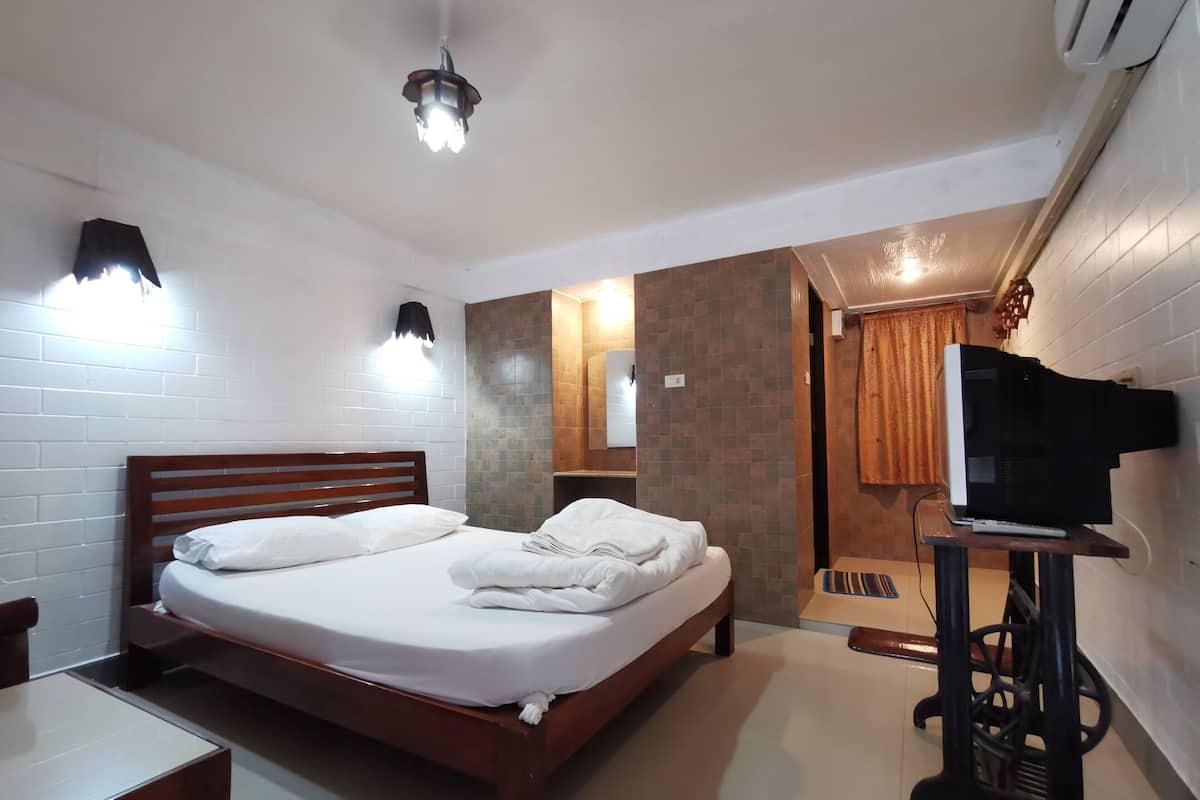 Een hotelkamer met een houten bed, witte wanden, een betegelde douche en een wandgemonteerde televisie.
