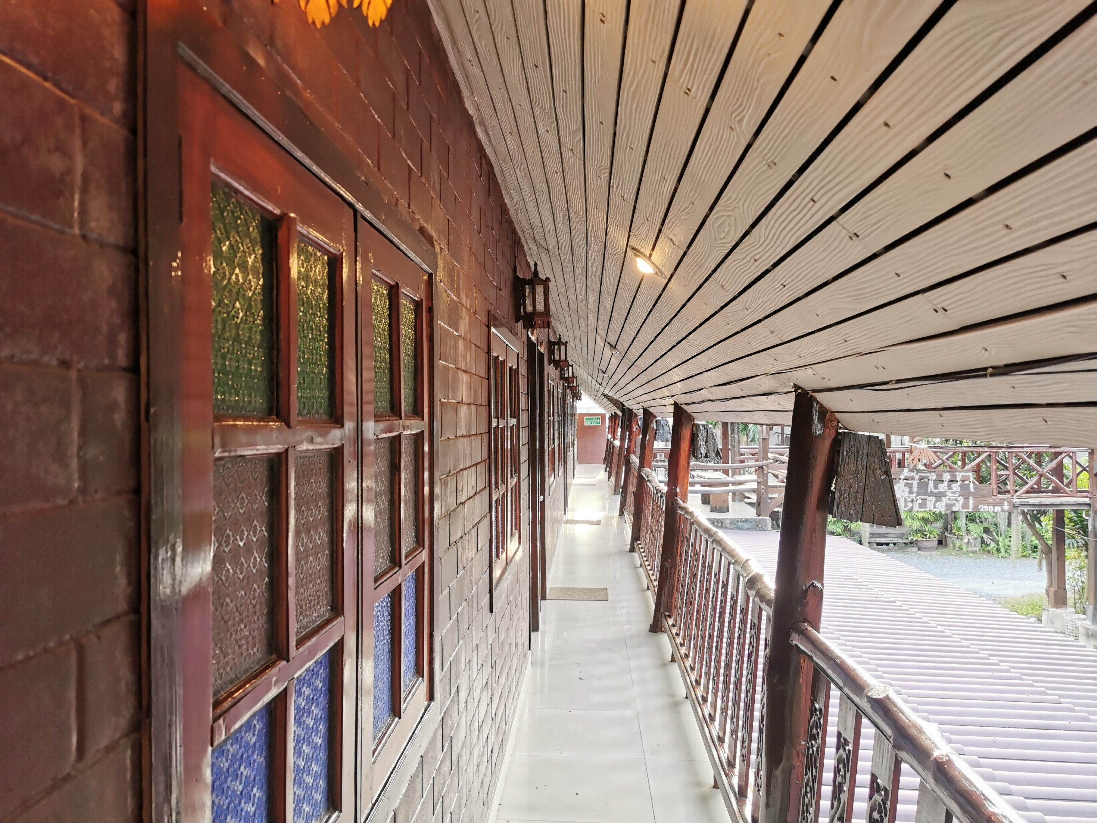 A covered corridor with wooden railings, patterned windows, and a tiled floor.