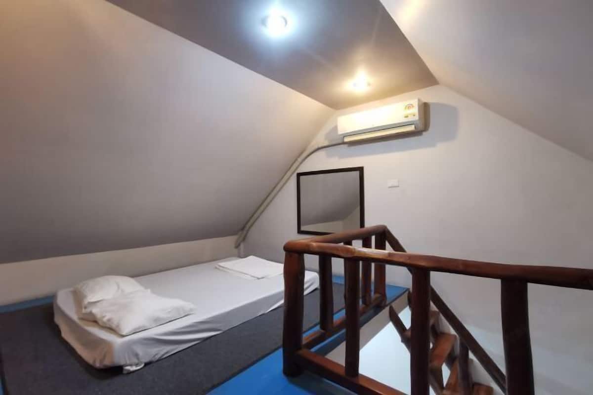 Een kleine kamer met een enkel bed, een houten leuning, een airconditioner en een plafondlamp.