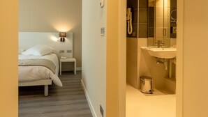 A hotel room with a bed, bedside table, and a bathroom with a sink and mirror. - La Dolce Vita Hotel (Menton)