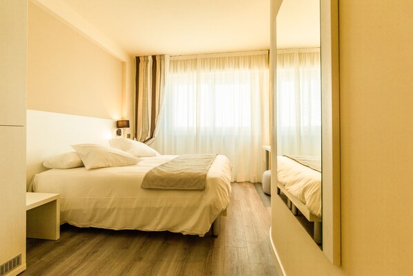 Ein Hotelzimmer mit Bett, Nachttisch und einem Fenster mit Vorhängen.