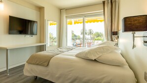 A hotel room with a bed, a TV mounted on the wall, a window with curtains, and a balcony with outdoor furniture. - La Dolce Vita Hotel (Menton)