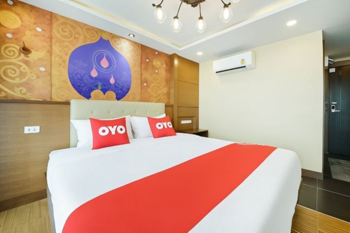 A hotel room with a large bed, a wall mural, an air conditioning unit, and a door to the right.