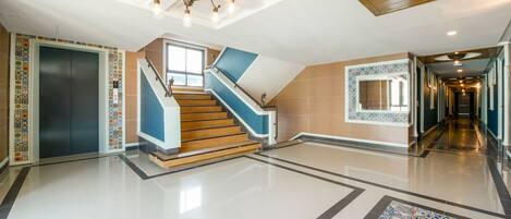 A spacious lobby with a modern staircase, a decorative ceiling light, and a patterned floor.