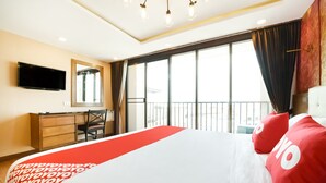 Habitación de hotel con una cama grande, un escritorio, una silla, un televisor y un balcón con vistas.