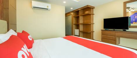 A hotel room with a bed, a TV, a wardrobe, and an air conditioning unit.